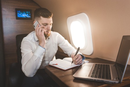 Young attractive and successful businessman talking on the phone and working while sitting in the...