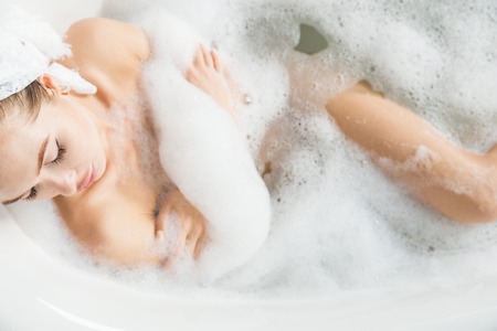 A young attractive girl relaxes in the bathroom and rests against the backdrop of a beautiful light interior. Spa treatments for beauty and health with skin careの写真素材