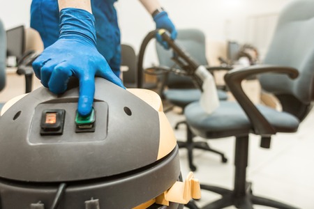 Young man in workwear and rubber gloves cleans the office chair with professional equipment.の写真素材