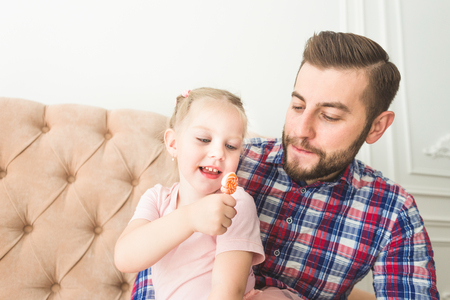 Cute little girl with a lollipop sitting with dad on the couch.の写真素材