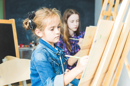 little girl with a teacher in group of preschool student sat the drawing a picture. Painting on maelbert, palette and paints. Back to school and Education concept.の写真素材