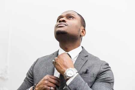 Young African American businessman in a gray suit tying a tie on a white background.の写真素材