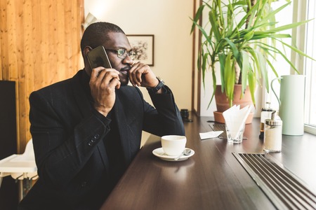 Young handsome dark-skinned businessman in a cafe talking on a cell phone with a cup of tea.の写真素材
