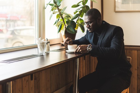 Young handsome dark-skinned businessman drinks coffee in a cafe.の写真素材