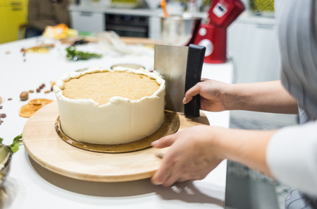Confectioner smooths white cream on a biscuit cake with a cooking spatula. The concept of homemade pastry, cooking cakes.の写真素材