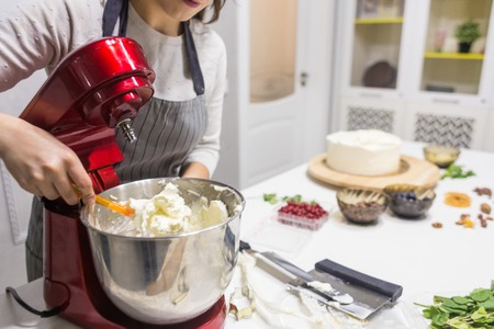 Young female confectioner whips cream in a metal bowl in a red electric mixer. The concept of homemade pastry, cooking.の写真素材