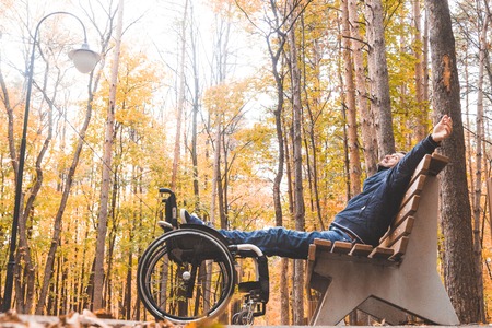 Young man resting sitting on a bench with his legs on his wheelchair.の写真素材