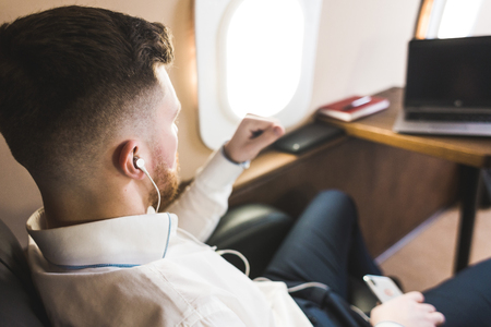 Young attractive and successful businessman is resting and listening to music works while sitting in the chair of his private business planeの写真素材