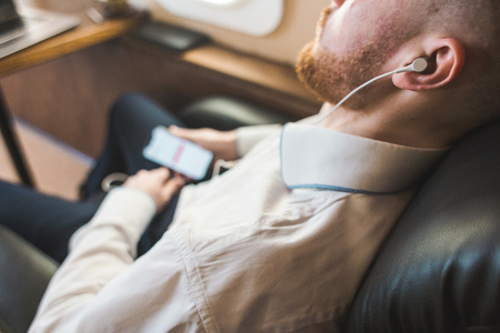 Young attractive and successful businessman is resting and listening to music works while sitting in the chair of his private business planeの写真素材