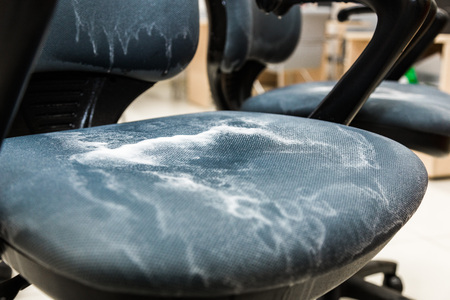 Young man in workwear and rubber gloves cleans the office chair with professional equipment.の写真素材