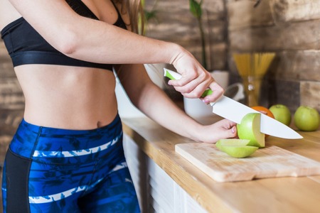Attractive girl in sportswear preparing a healthy breakfast in the kitchen before training, cutting fruit and making fresh juice. Healthy lifestyle, fitness and beautの写真素材