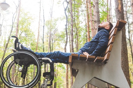 Young man resting sitting on a bench with his legs on his wheelchair.