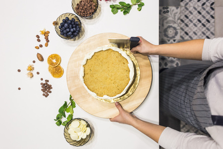 Confectioner smooths white cream on a biscuit cake with a cooking spatula. The concept of homemade...