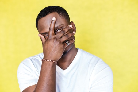 African American man covering face with hand and looking at cameraの写真素材