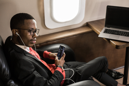 Successful young Afro American black businessman sitting in the chair of his private jetの写真素材