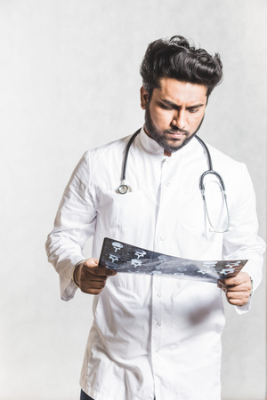 Handsome young doctor in a white coat with a stethoscope attentively checks the patients x-ray.の写真素材