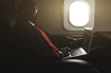 Attractive and successful African American businessman with glasses working on a laptop while sitting in the chair of his private jetの写真素材