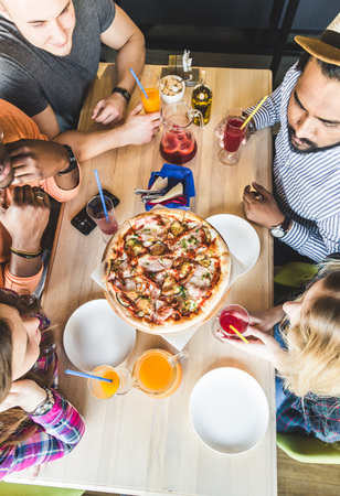 A company of multicultural  young people in a cafe eating pizza, drinking cocktails, having funの写真素材