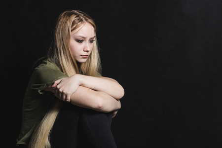 Sad young woman going to cry in a black backgroundの写真素材