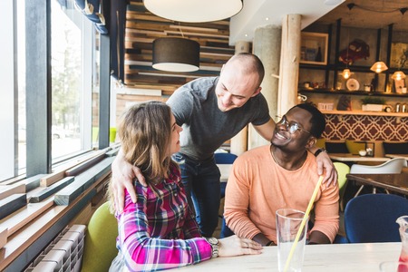 a group of young cheerful friends are sitting in a cafe, eating, drinking drinks, take selfies and take pictures. meeting, handshake and hugsの写真素材