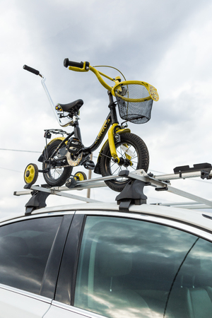 Bicycle transportation - a childrens bicycle on the roof of a car against the sky in a special mount for cycling. The decision to transport large loads and travel by carの写真素材