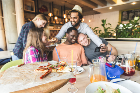 A company of multicultural  young people in a cafe eating pizza, drinking cocktails, having fun