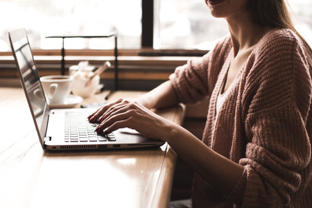 Attractive young woman sits at a table in a cafe with a cup of coffee and enjoys a laptopの写真素材