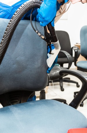Young man in workwear and rubber gloves cleans the office chair with professional equipment.の写真素材