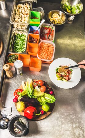 Professional chef cooking in the kitchen restaurant at the hotel, preparing dinner. A cook in an apron makes a salad of vegetables and pizzaの写真素材