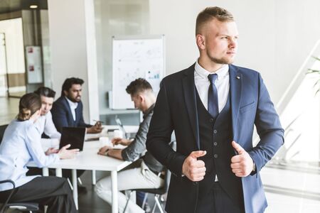 Business man stands on the background of partners. A team of young businessmen working and communicating together in an office. Corporate businessteam and manager in a meeting.の写真素材
