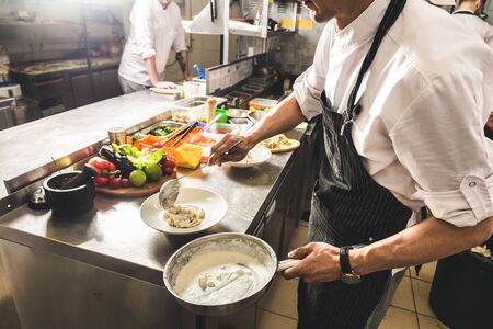 Professional chef cooking in the kitchen restaurant at the hotel, preparing dinner. A cook in an...