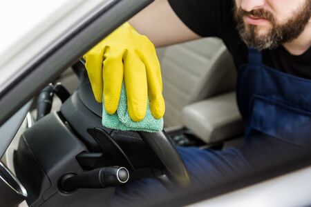 Cleaning service. Man in uniform and yellow gloves washes a car interior in a car wash.の写真素材