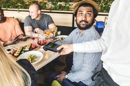 Young attractive Hindu man paying in cafe with contactless smartphone paymentの写真素材
