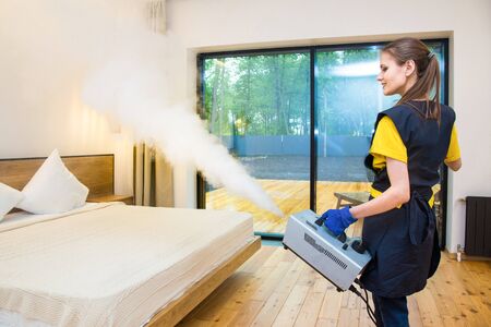 professional cleaning service. woman in uniform and gloves does the cleaning in a cottage. treatment, disinfection of the apartment with hot steam from odors and parasites, bed bugsの写真素材