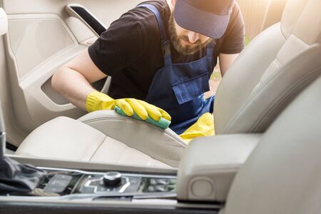 Cleaning service. Man in uniform and yellow gloves washes a car interior in a car wash. Worker washes the chairs of the leather salonの写真素材
