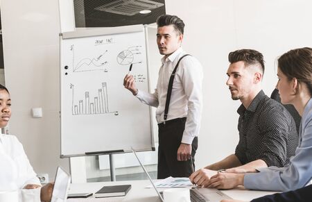 Company leader standing near the flipchart. A team of young businessmen working and communicating together in an office. Corporate businessteam and manager in a meetingの写真素材