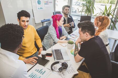 Group of multi ethnic executives discussing during a meeting. Business man and woman sitting around table at office and smiling. A team of young creative designersの写真素材