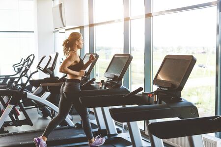 The athletic woman dressed in a black sportswear running on the treadmill in the modern gym