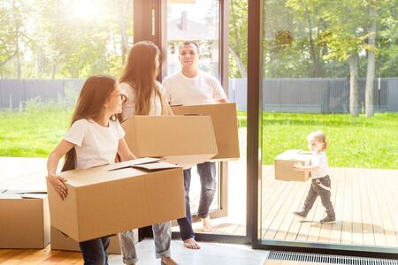 Happy young family, parents daughter and son, unpacking boxes and moving into a new home. funny kids run in with boxesの写真素材