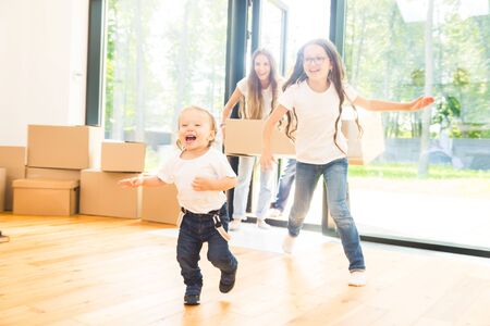 Happy young family, parents daughter and son, unpacking boxes and moving into a new home. funny kids run in with boxesの写真素材