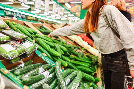 Shopping at the supermarket. The girl in the store picks cucumbers in the vegetable department. A healthy and balanced dietの写真素材