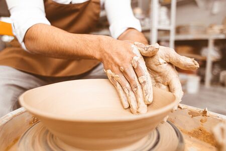 A young male potter works in his workshop on a potter's wheel and makes clay products. Close-up of hands.の写真素材