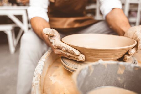 A young male potter works in his workshop on a potter's wheel and makes clay products. Close-up of hands.の写真素材