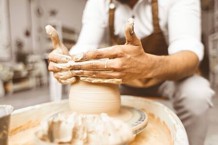 A young male potter works in his workshop on a potter's wheel and makes clay products. Close-up of hands.の写真素材