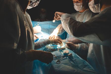 An international professional team of surgeon, assistants and anesthesiologist perform a complex operation on a patient under general anesthesia. Dark atmospheric photography theme in low keyの写真素材
