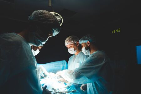 An international professional team of surgeon, assistants and anesthesiologist perform a complex operation on a patient under general anesthesia. Dark atmospheric photography theme in low keyの写真素材