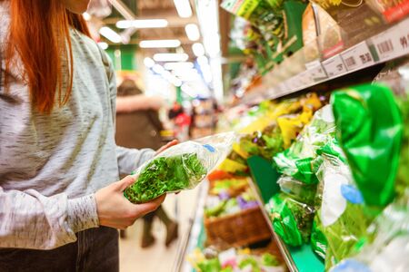 Shopping at the supermarket. The girl in the store chooses a salad in the vegetable department. A...