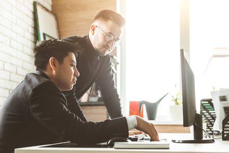 Young office worker sitting at desk, using computer. Two business man talkingの写真素材