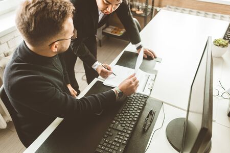 Young office worker sitting at desk, using computer. Two business man talking.の写真素材
