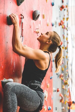 Sportswoman climber moving up on steep rock, climbing on artificial wall indoors. Extreme sports and...